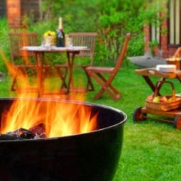 Lit barbecue pit in a back yard with a dinner table and food cart.